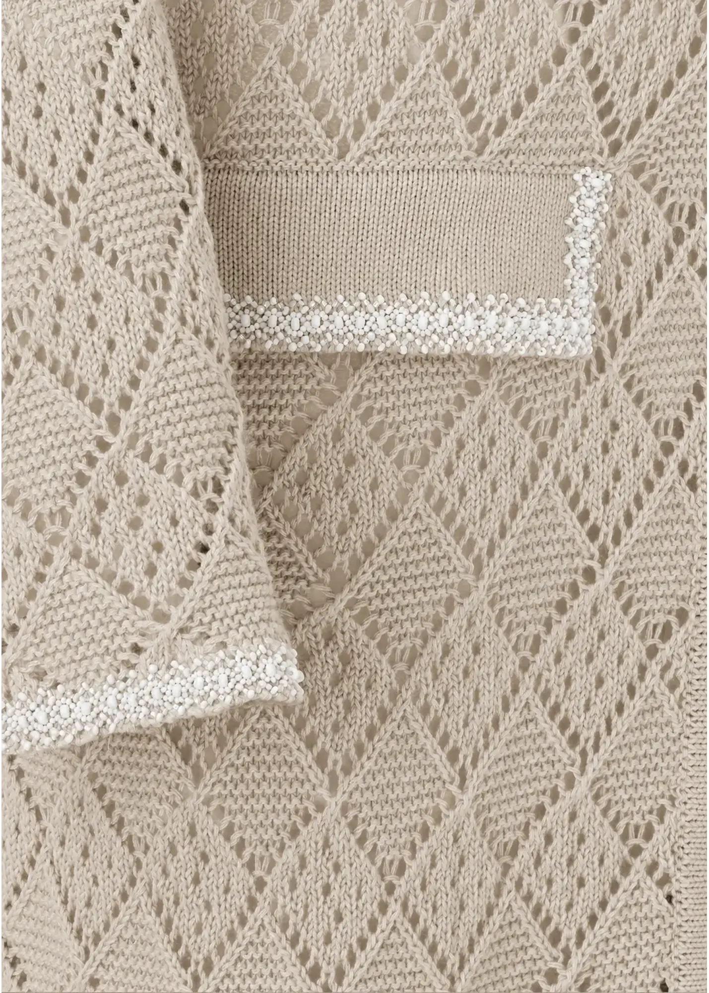 Close-up detail of a luxury cotton knit cardigan featuring an intricate openwork geometric knit pattern, textured trim detailing on the pocket and cuff, and refined artisanal craftsmanship in a soft natural beige tone.
