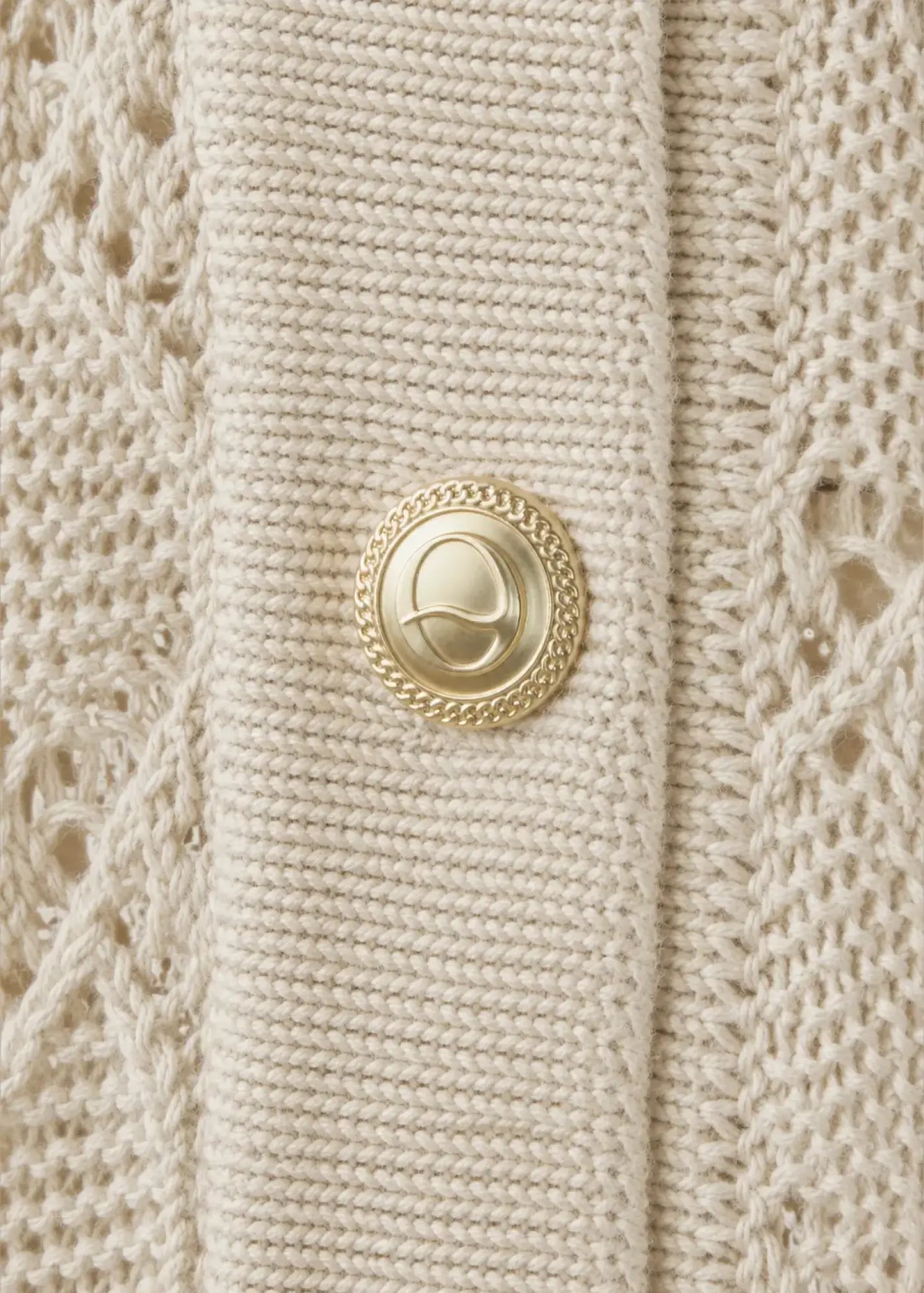Close-up of a luxury cotton knit cardigan featuring an intricate openwork pattern, refined rib-knit placket, and an elegant gold-tone signature button, highlighting exceptional craftsmanship and premium detailing.