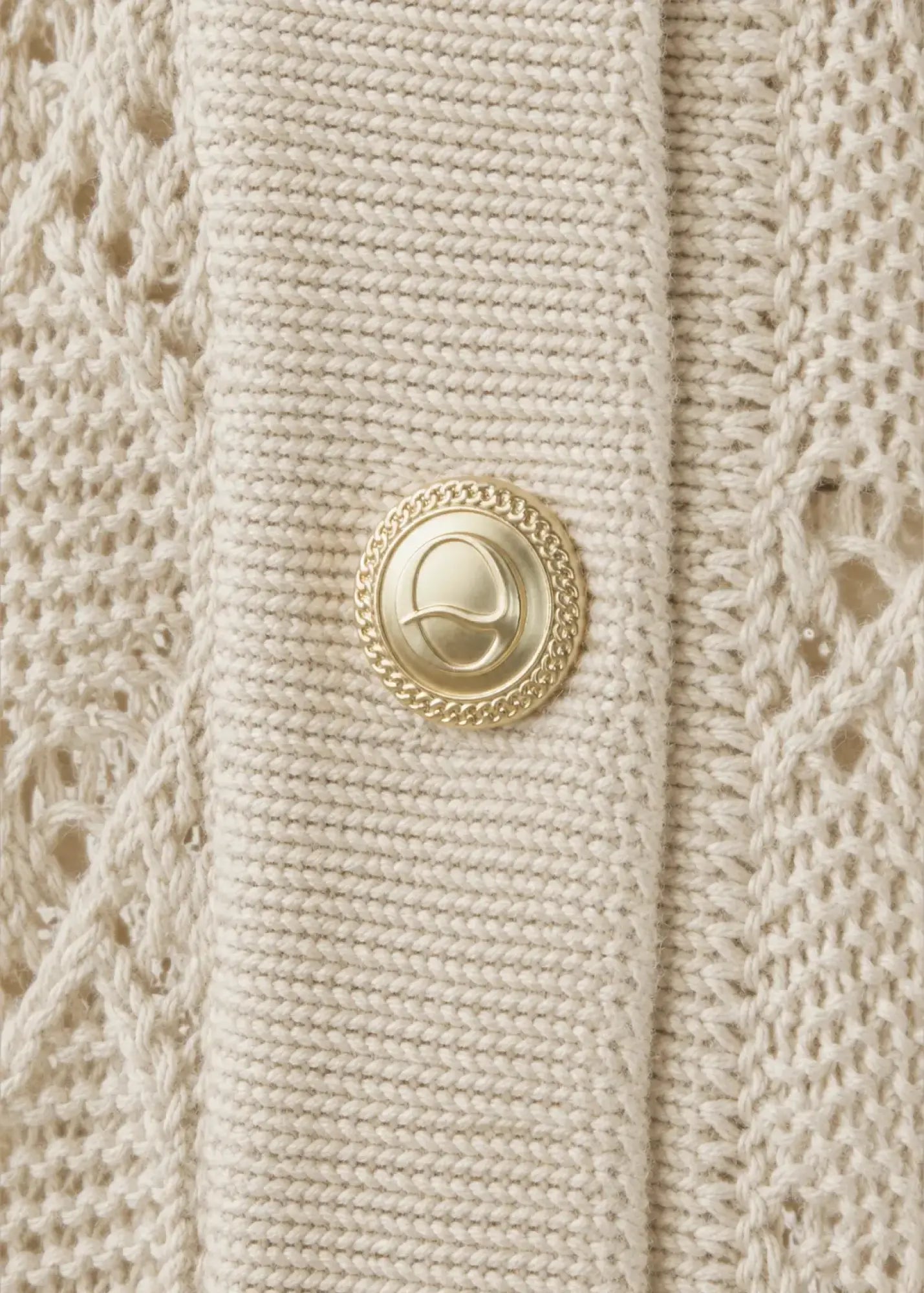 Close-up of a luxury cotton knit cardigan featuring an intricate openwork pattern, refined rib-knit placket, and an elegant gold-tone signature button, highlighting exceptional craftsmanship and premium detailing.
