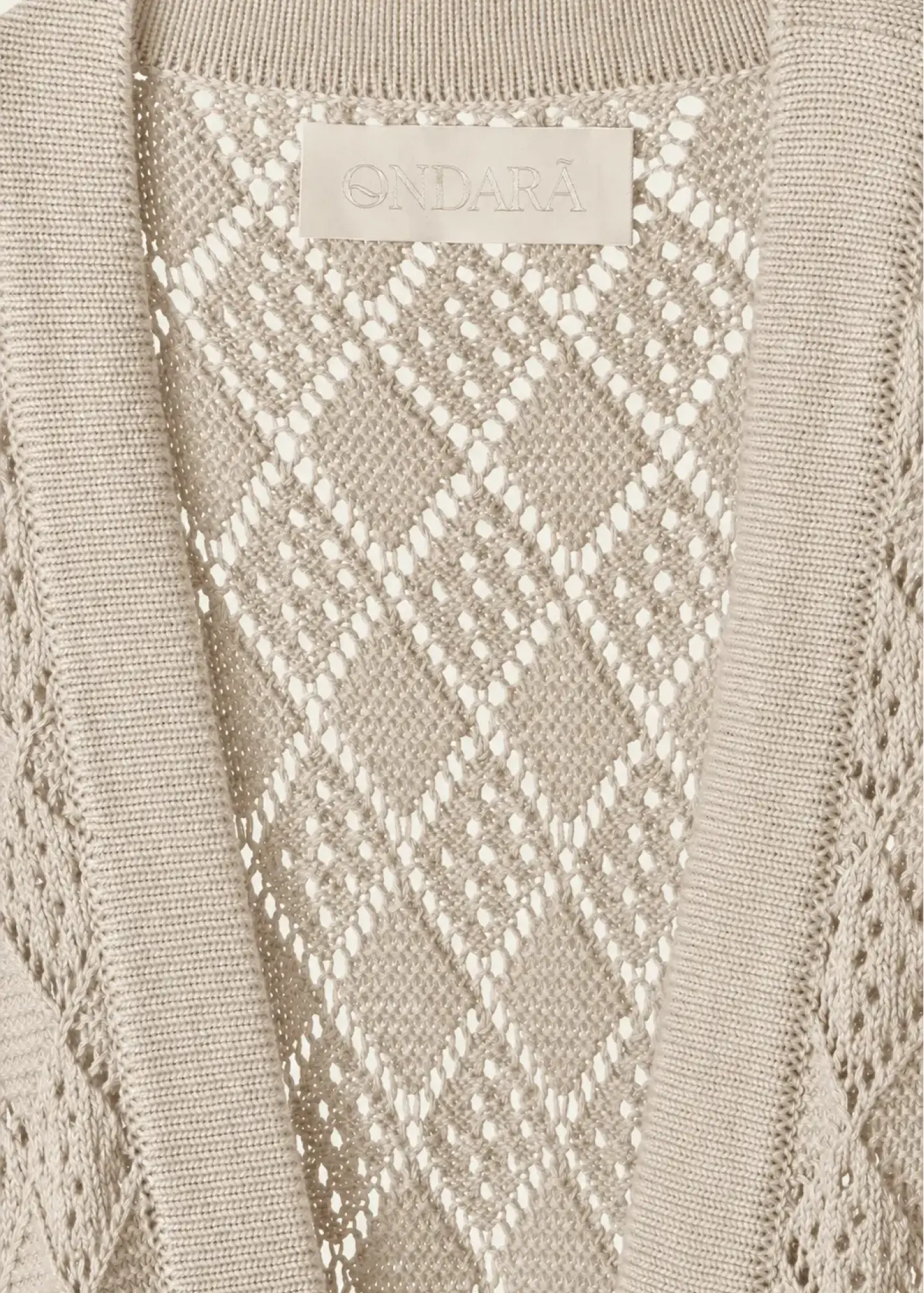 Close-up of a luxury cotton knit cardigan showcasing an intricate openwork diamond pattern, refined rib-knit trim, and a tonal Ondará signature label, highlighting the garment’s artisanal craftsmanship and lightweight construction.