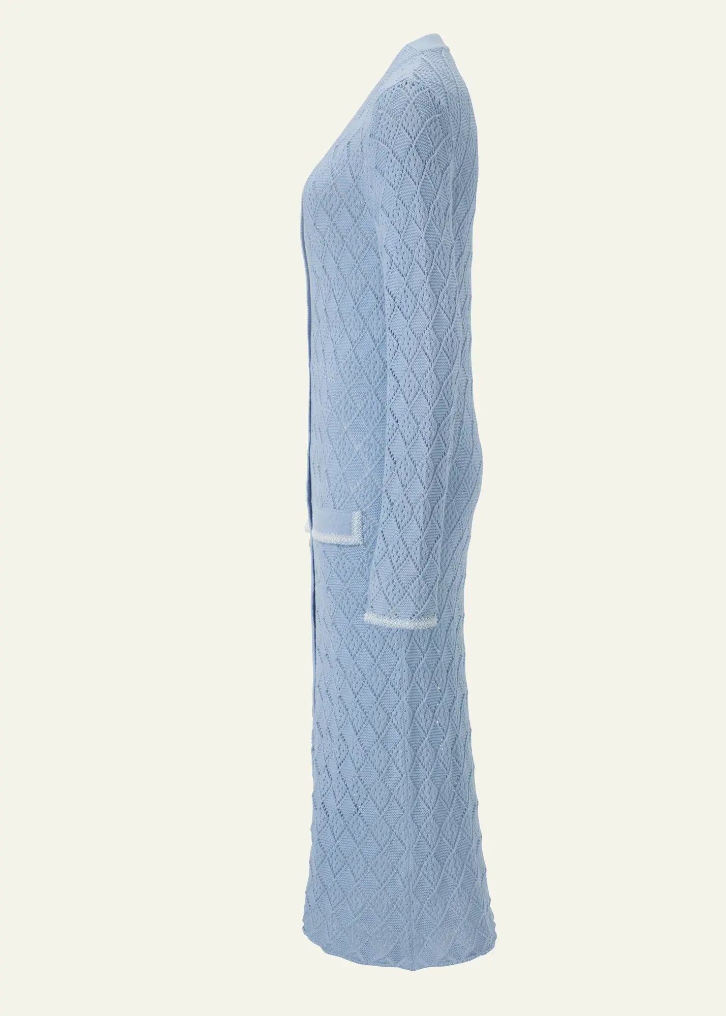 Side view of a luxury women's cardigan dress in soft sky-blue fine cotton, featuring an intricate geometric openwork knit pattern, elongated silhouette, refined pocket detailing, and artisanal craftsmanship.