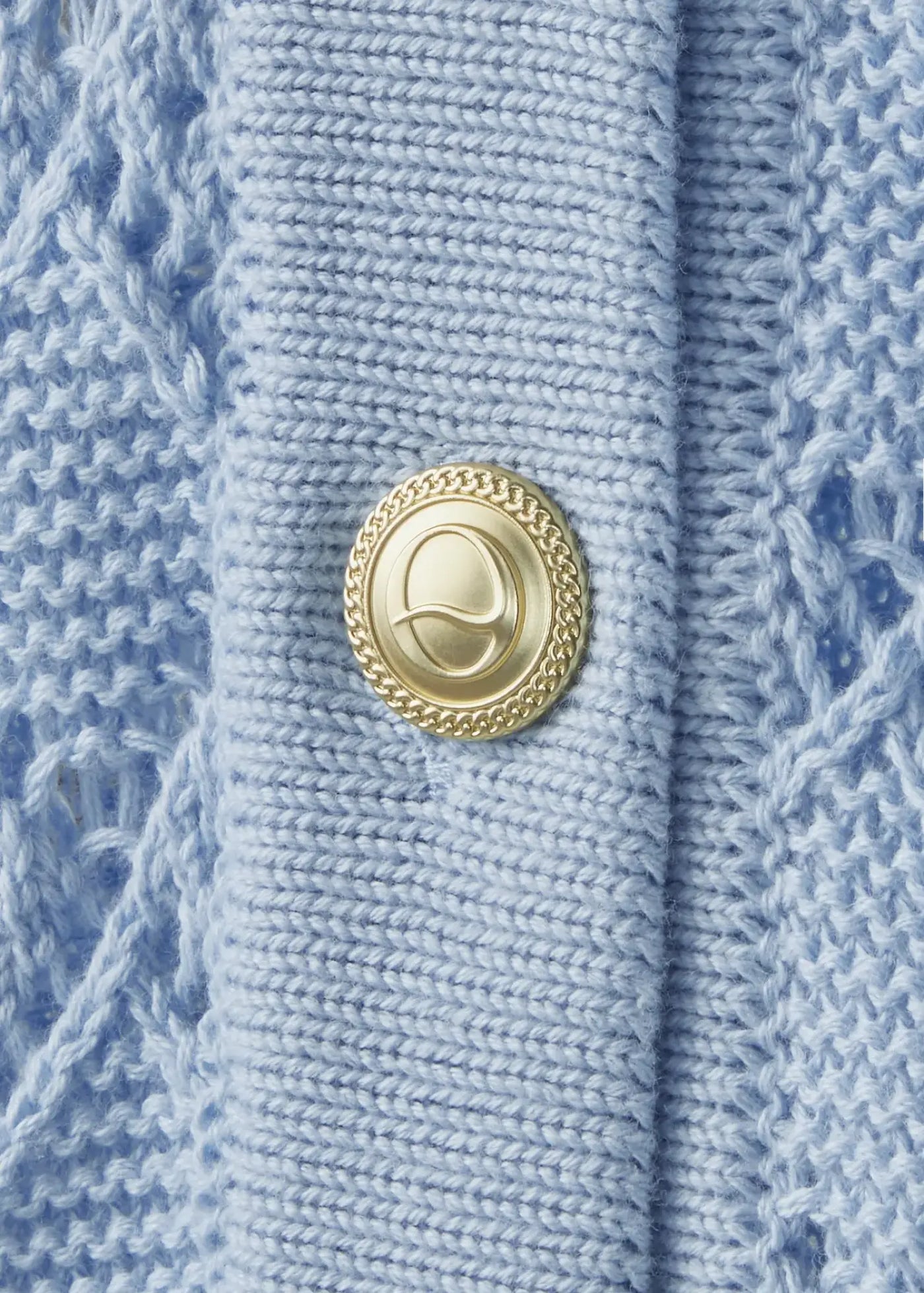 Detailed view of the signature Ondará gold-tone button on a luxury sky-blue cotton knit cardigan, highlighting premium craftsmanship and elegant finishing details.
