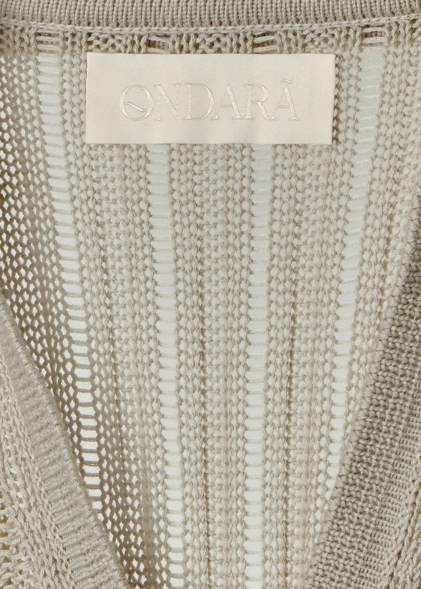 Close-up of a luxury fine cotton knit dress featuring an intricate openwork stripe pattern, lightweight breathable construction, and a tonal Ondará signature label, showcasing refined craftsmanship and elegant detailing.