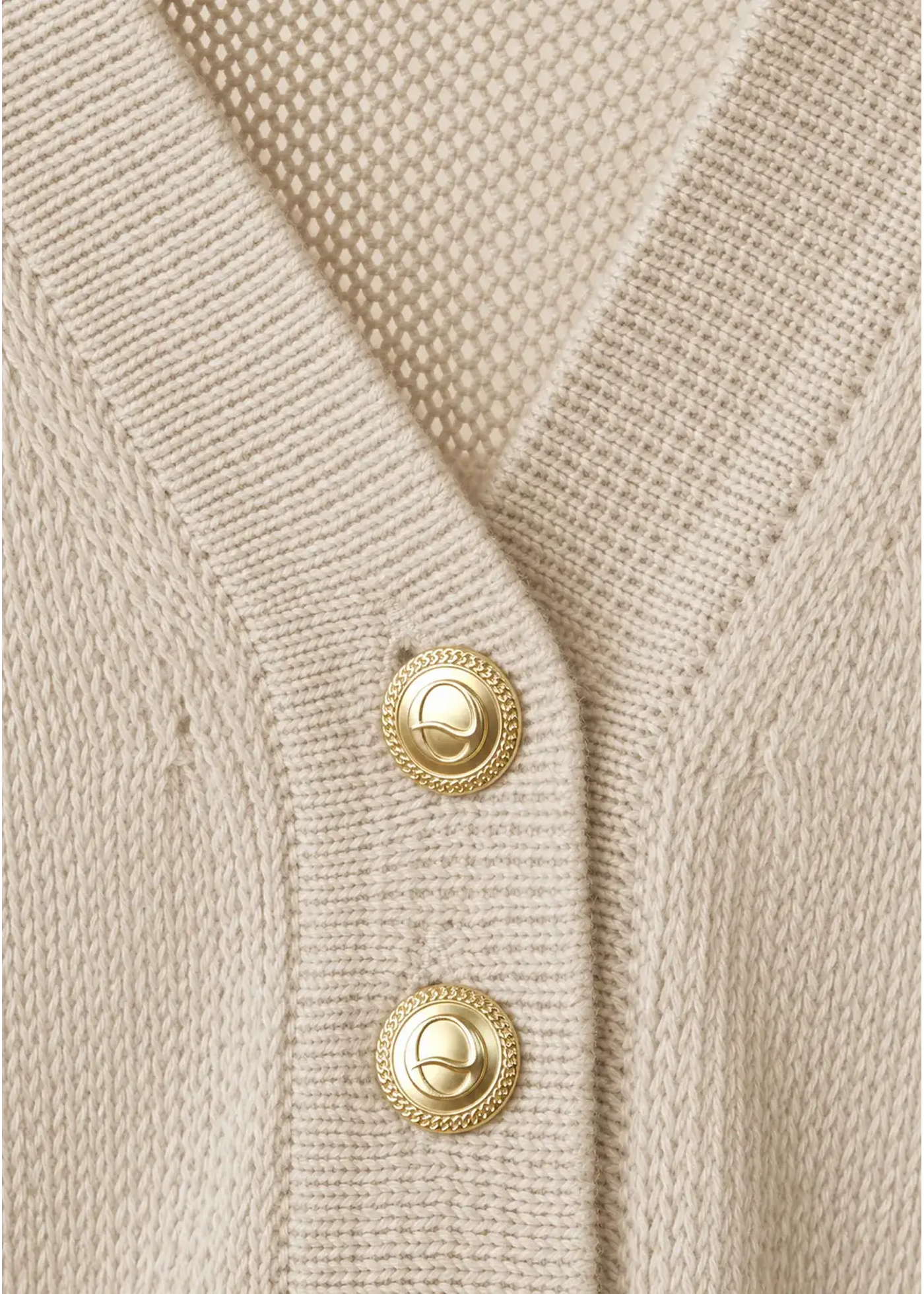 Close-up of a luxury knit polo in soft beige cotton, featuring signature gold-tone logo buttons, a refined V-neck collar, and premium craftsmanship.
