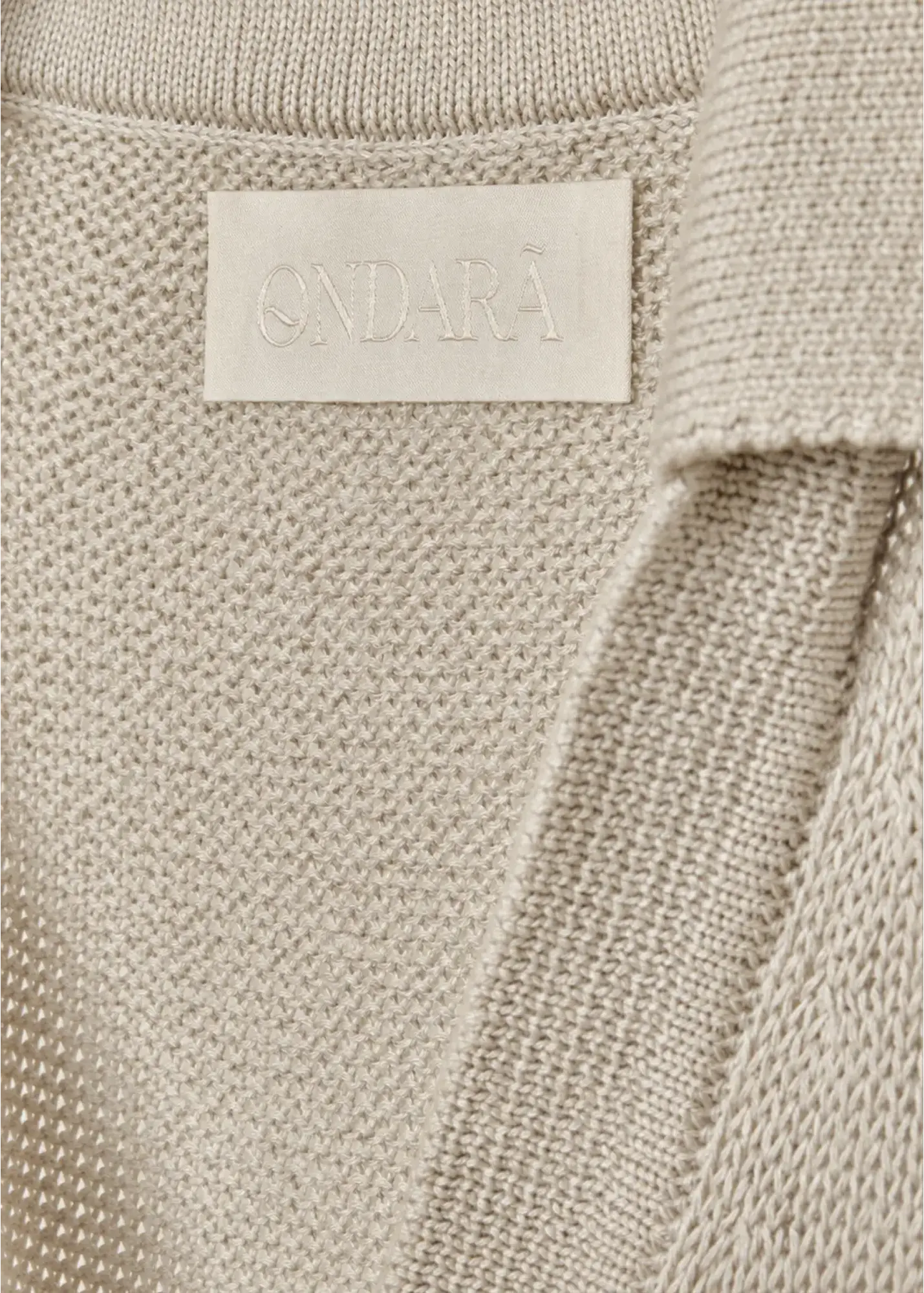 Luxury knitwear detail featuring a tonal Ondara woven label, textured cotton knit construction, and elegant minimalist design.