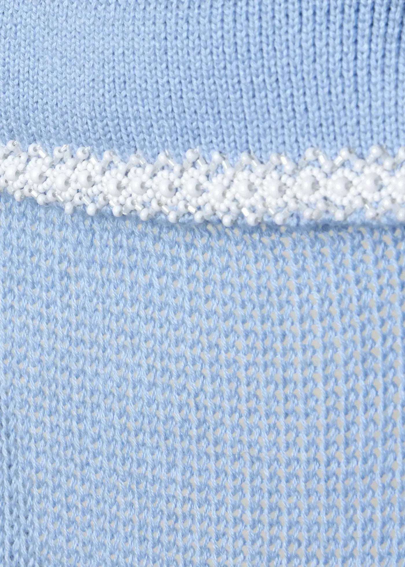 Close-up of delicate white beaded embellishment on soft sky-blue knitwear, showcasing luxurious craftsmanship and refined artisanal detailing.
