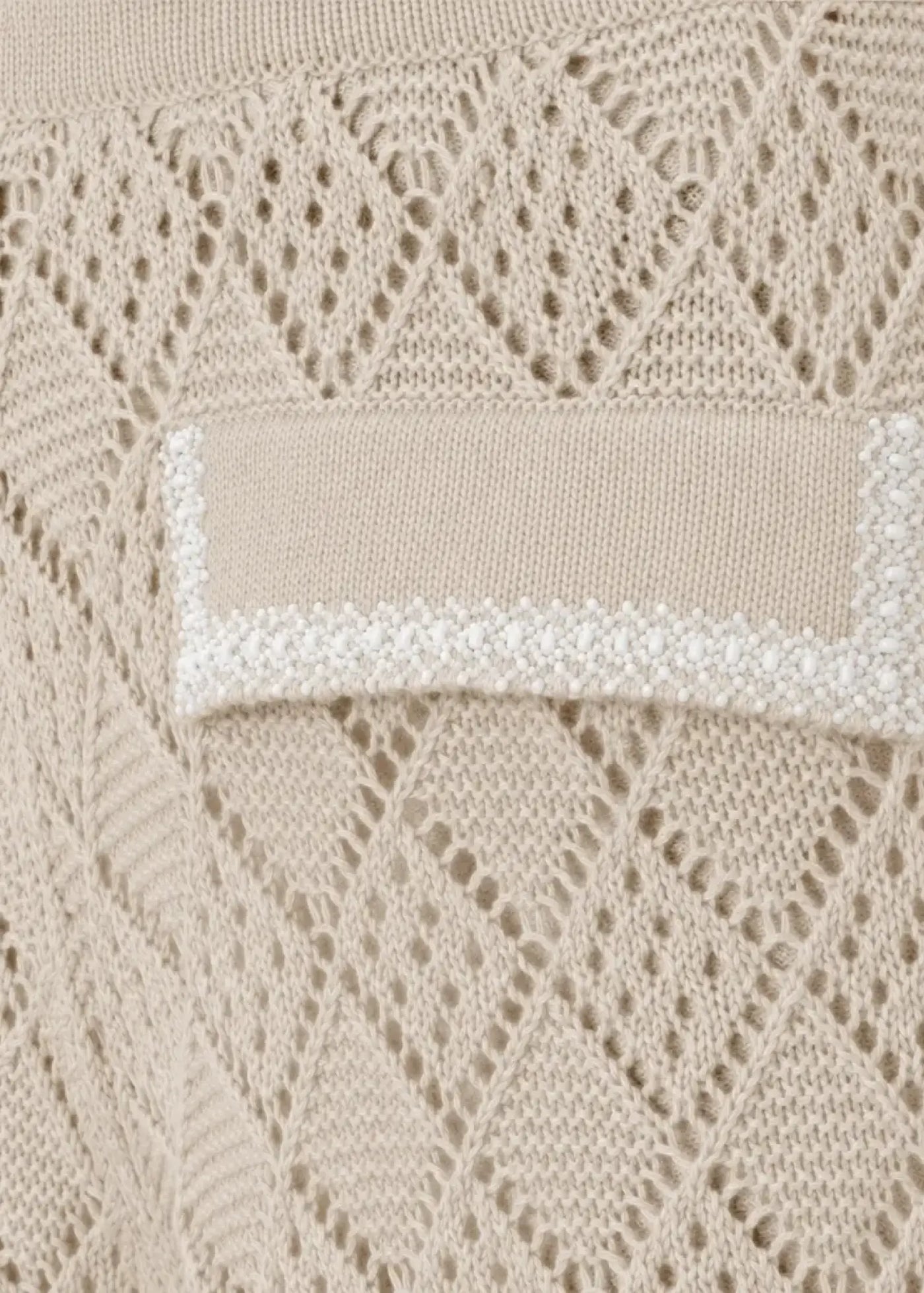 Close-up of luxury knit shorts in soft beige featuring an intricate openwork lace pattern and decorative pocket flap with hand-applied bead embellishments.