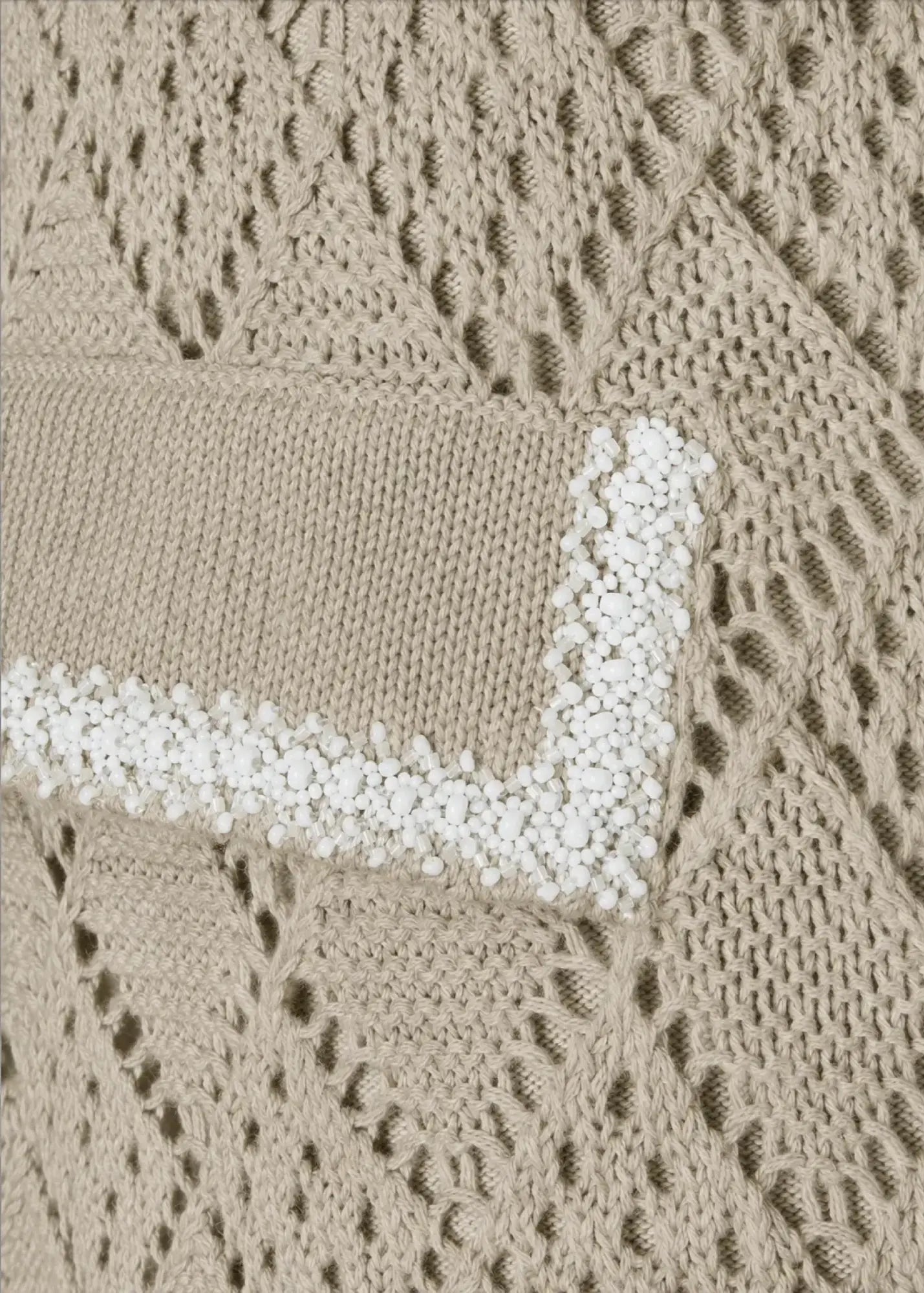 Close-up of luxury knit shorts in soft beige featuring intricate openwork patterns and a decorative pocket flap embellished with hand-applied white beads.