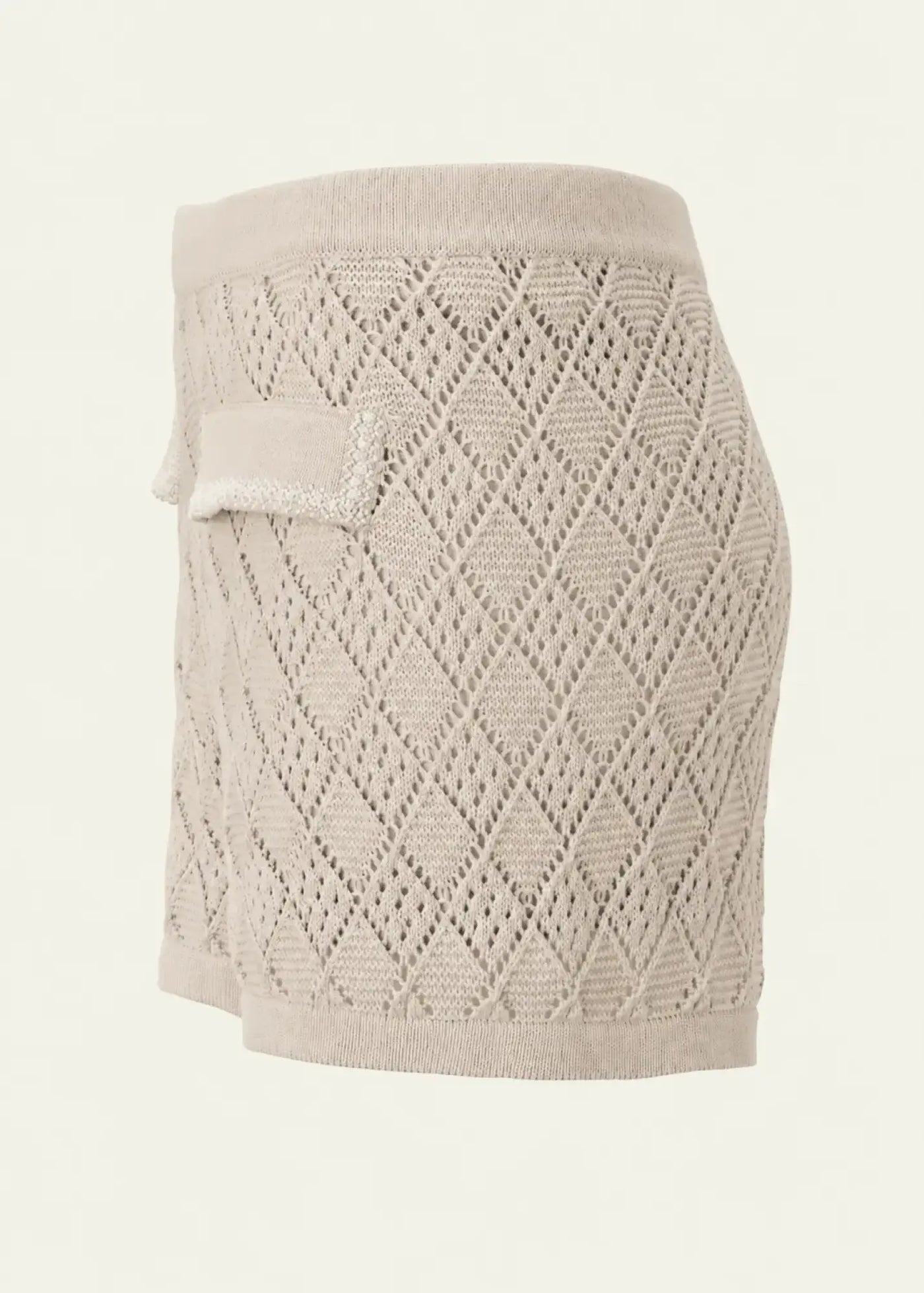 Luxury women’s knit shorts in soft beige, viewed from the side, featuring an intricate openwork diamond pattern and decorative pocket flap detailing.