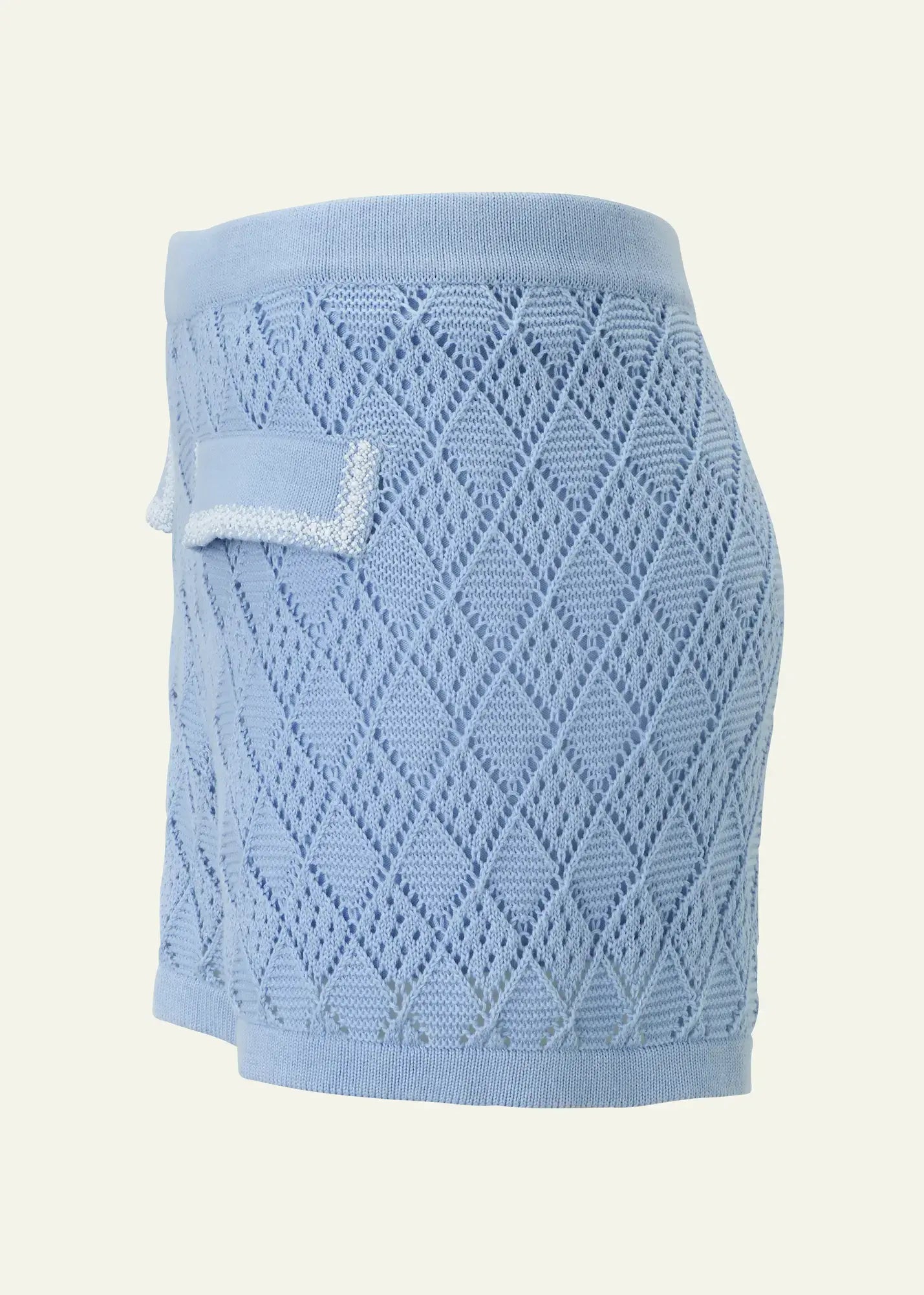 Luxury women’s crochet knit shorts in soft sky blue cotton, featuring an intricate openwork diamond pattern, a comfortable elastic waistband, and decorative flap pocket details with delicate white bead embellishments. Lightweight designer beachwear by Ondara, crafted for elegant resort styling.